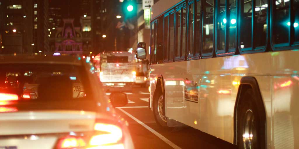 tilausajobussi ajaa liikenteessä henkilöauton vieressä pimeän aikaan